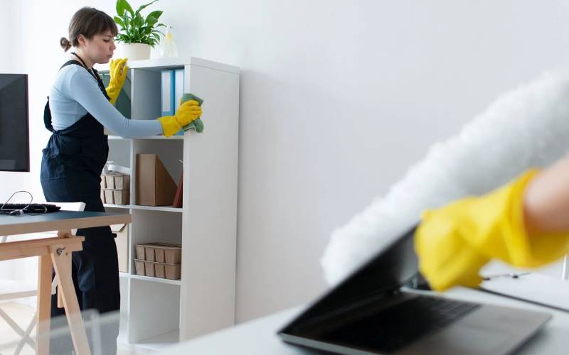 Professional cleaner dusting shelves in a commercial office