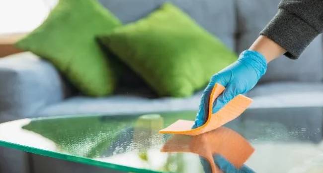 Professional cleaner wiping a glass table in a living area