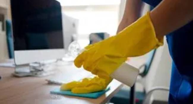 Professional cleaner wiping an office desk to improve workplace hygiene