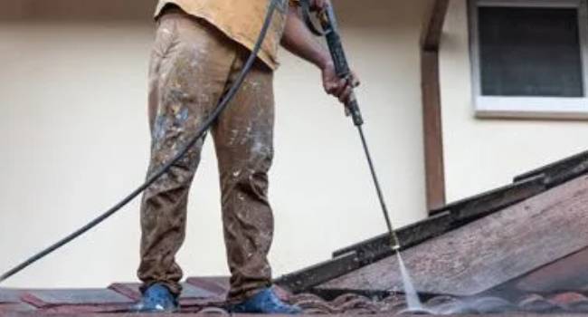 Professional cleaner power washing an exterior roof surface