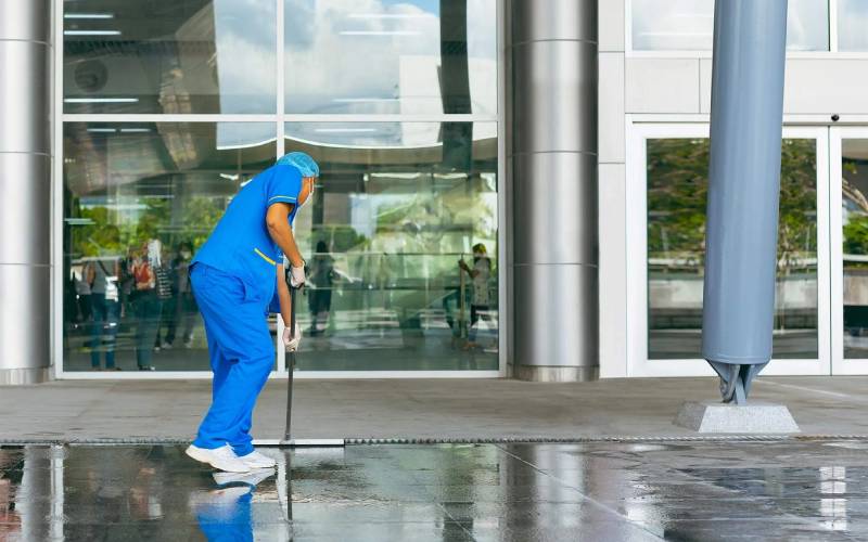 Professional cleaner using sustainable cleaning methods outside a commercial building